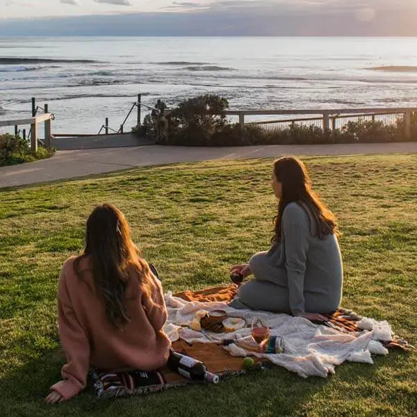 Deux femmes assises sur un plaid de camping qui sont installées face à la mer