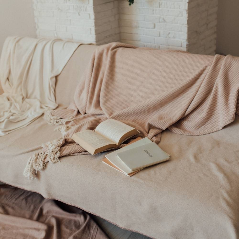 A sofa covered with a beige throw and a fringed dusty pink throw